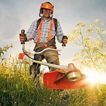 Best STIHL Petrol Strimmers in the UK: A Buyer’s Guide - A gardener using a STIHL petrol strimmer in a sunny field.