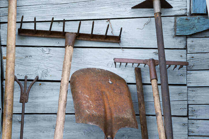 Keep Your Garden Tools Rust Free With These Tips: image of various garden tools hanging on a wooden wall, some showing signs of rust.