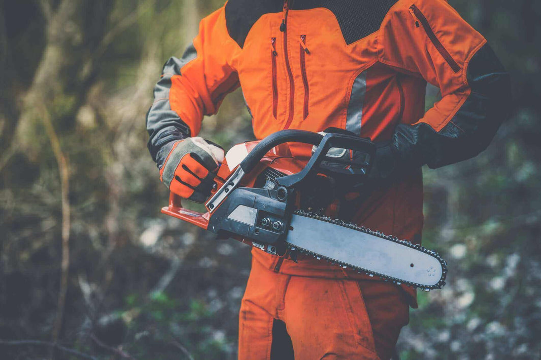 A person in safety gear holding a chainsaw, demonstrating safe practices while using garden machinery.
