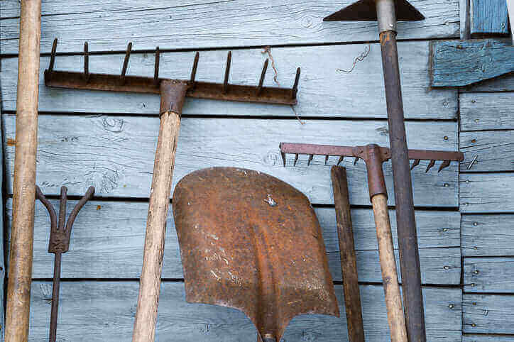 Keep Your Garden Tools Rust Free With These Tips: image of various garden tools hanging on a wooden wall, some showing signs of rust.