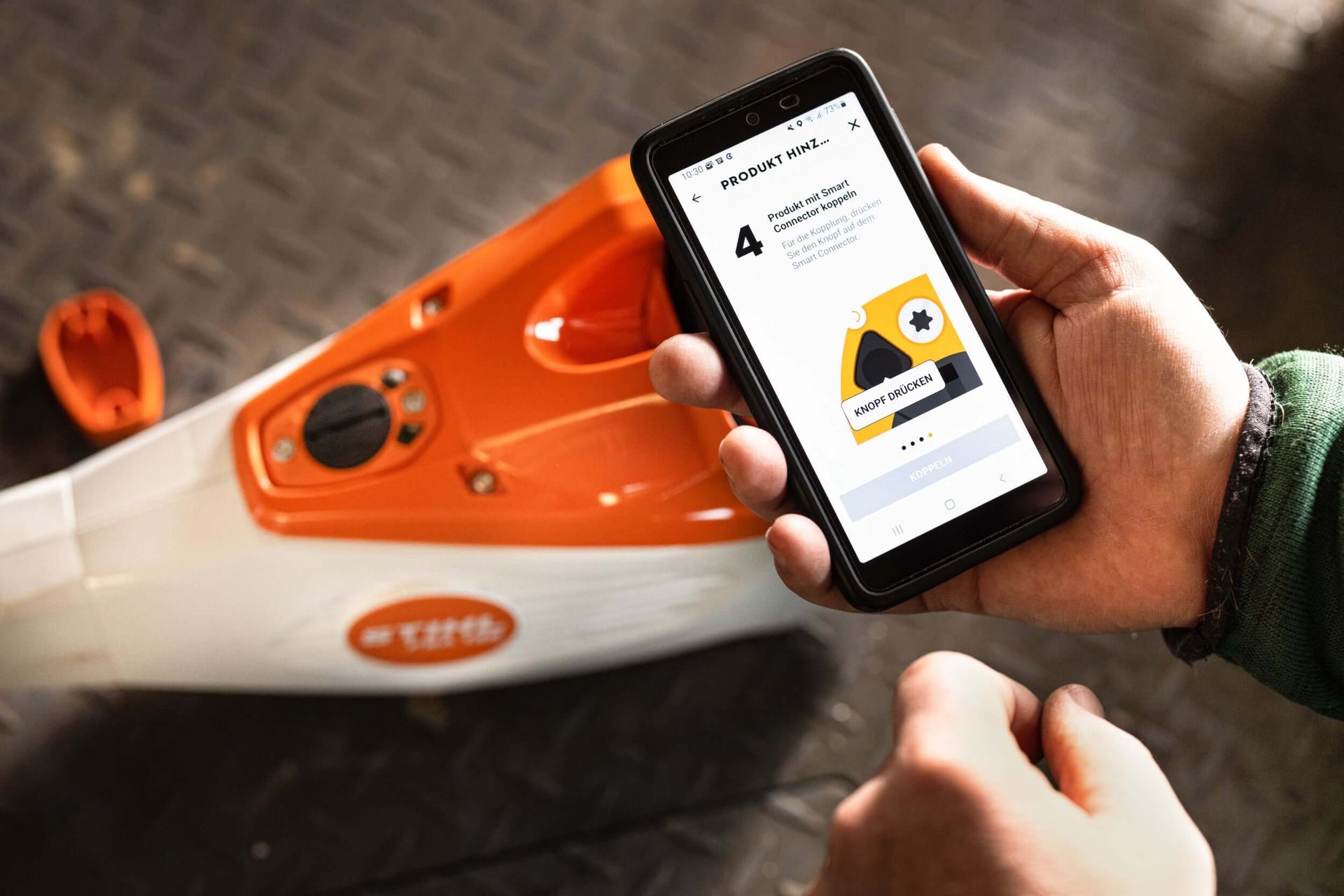 Person checking STIHL battery machine accessory information on a smartphone with chainsaw in background.