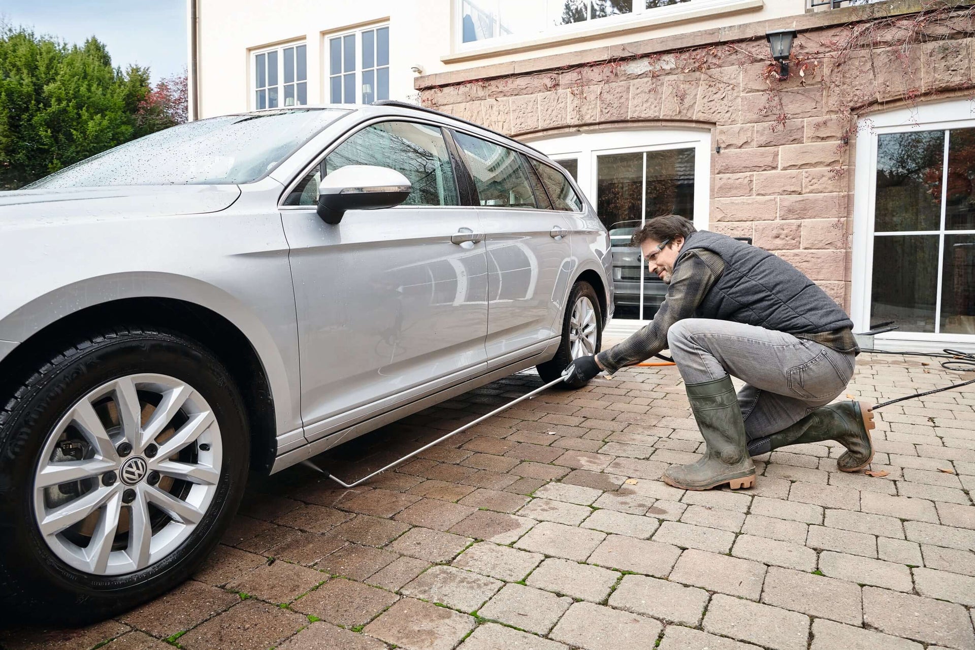 A person using a pressure washer to clean a car on a patio, demonstrating STIHL pressure washer accessories in action.