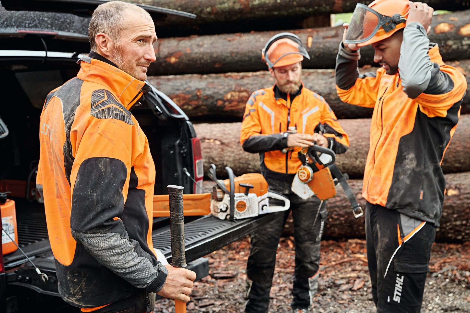 Tree surgeons in quality chainsaw PPE prepare for work amidst timber logs, showcasing safety gear and equipment.
