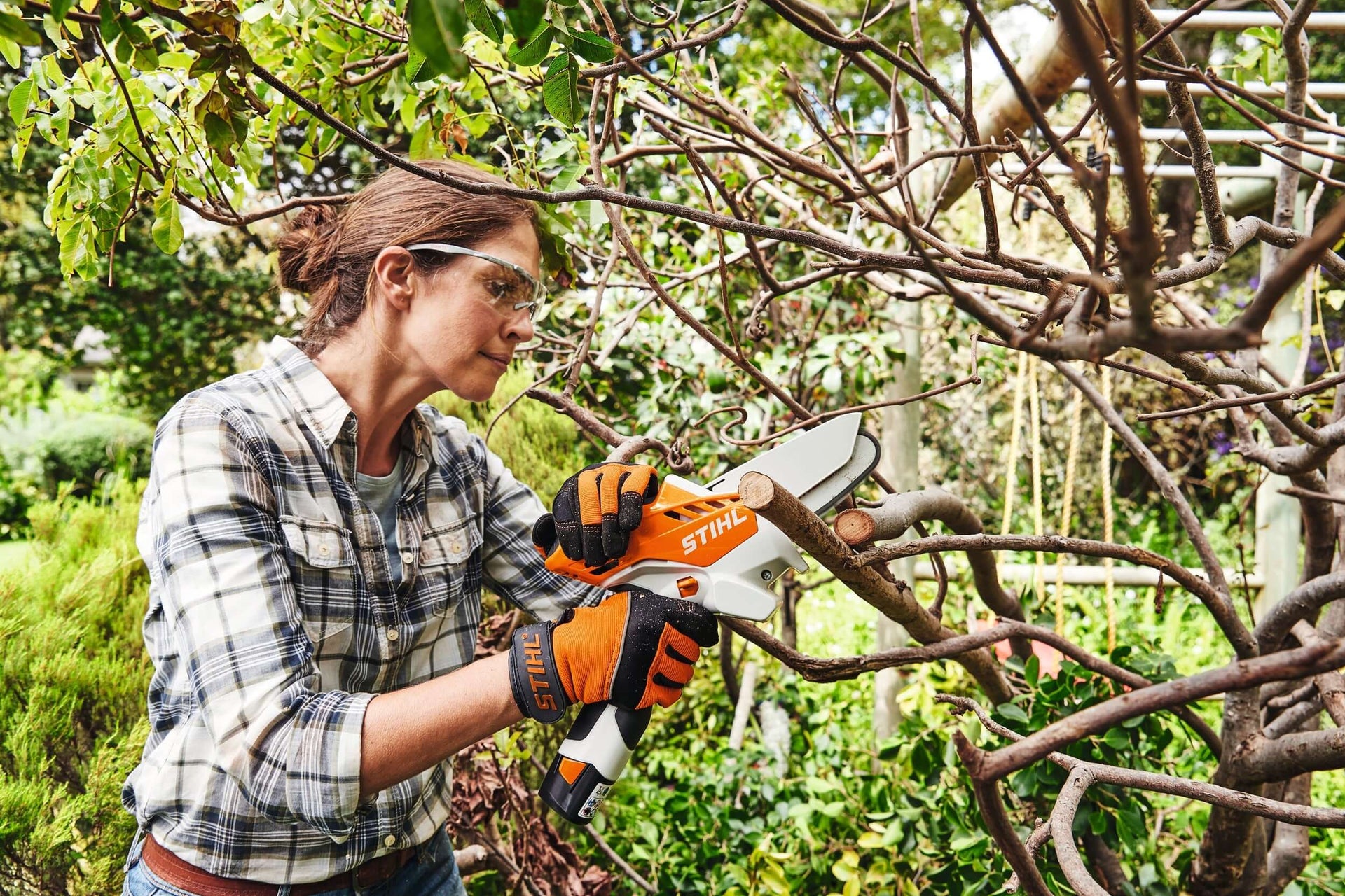 Woman using STIHL cordless secateurs for pruning trees, ideal for tree surgeons and garden maintenance enthusiasts.