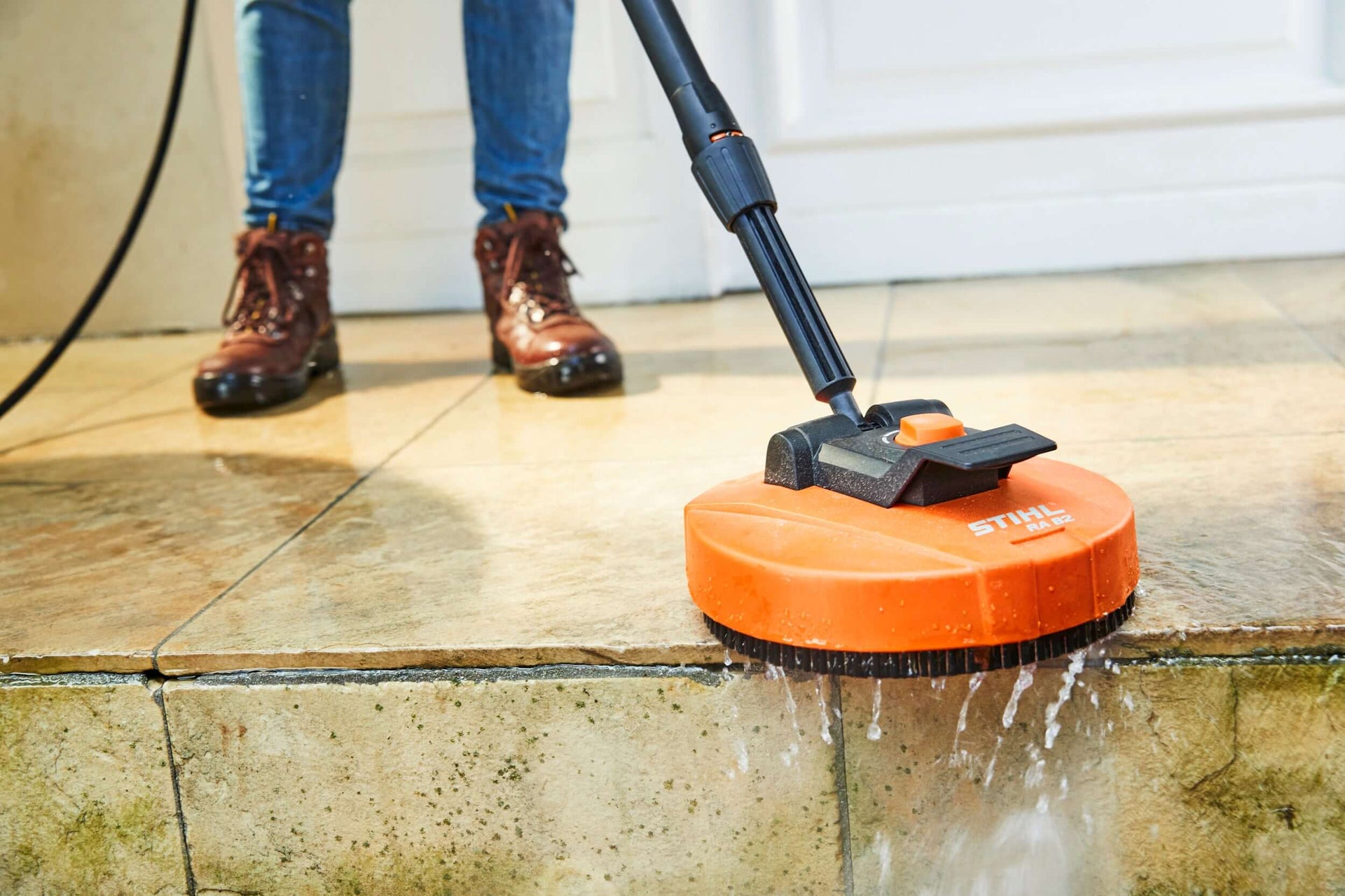 Person using a STIHL pressure washer attachment on dirty tiles, showcasing powerful cleaning performance.