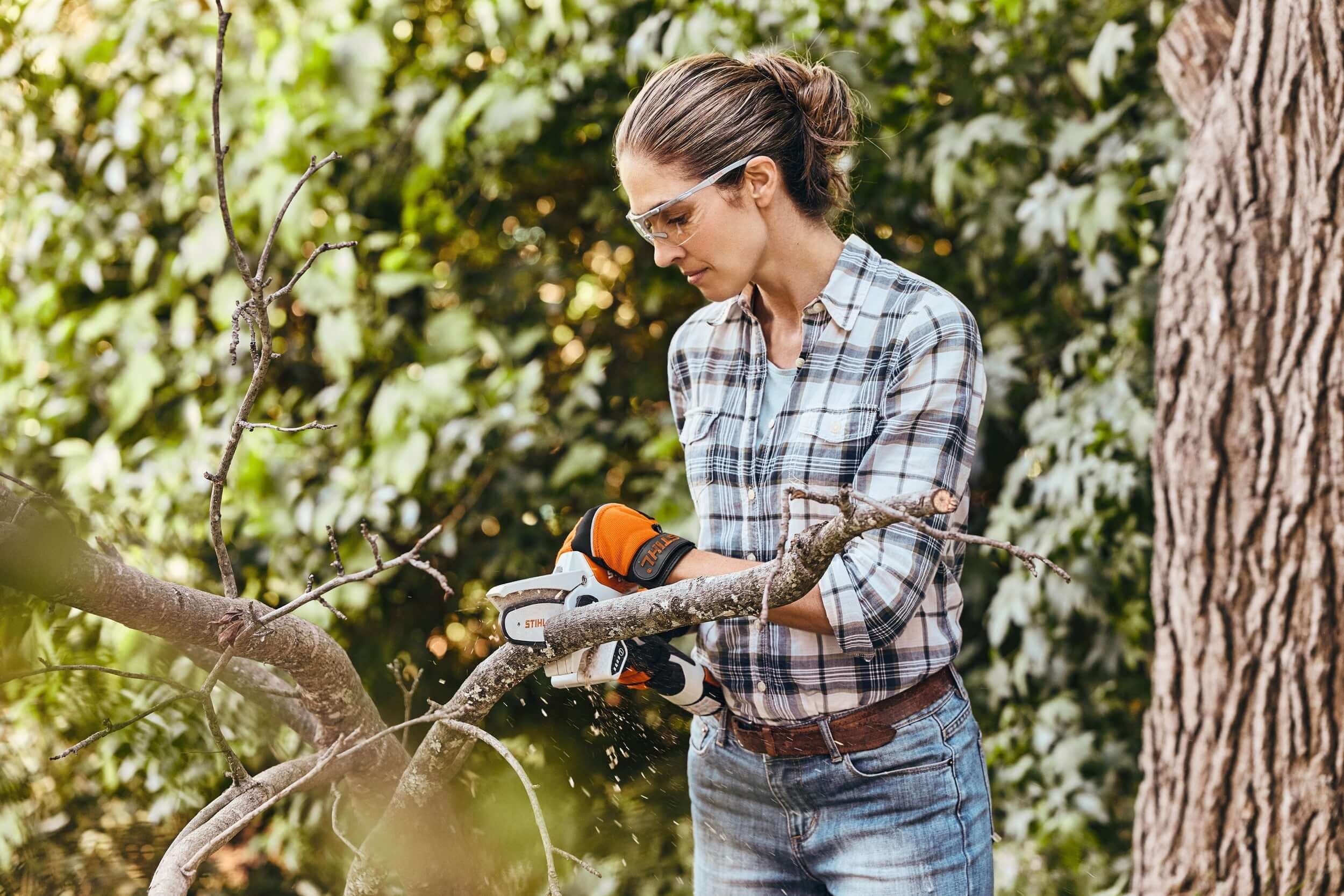 Woman using STIHL chainsaw to trim branches in a garden, embodying precision and strength for tree surgeons.