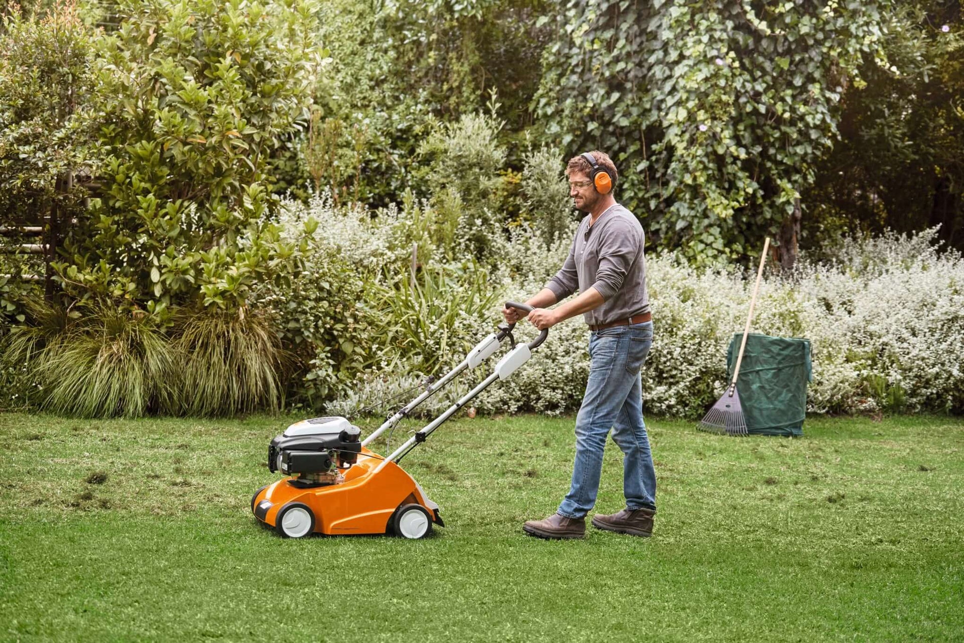 A man using a STIHL scarifier on a green lawn, promoting healthy grass growth and lawn care.