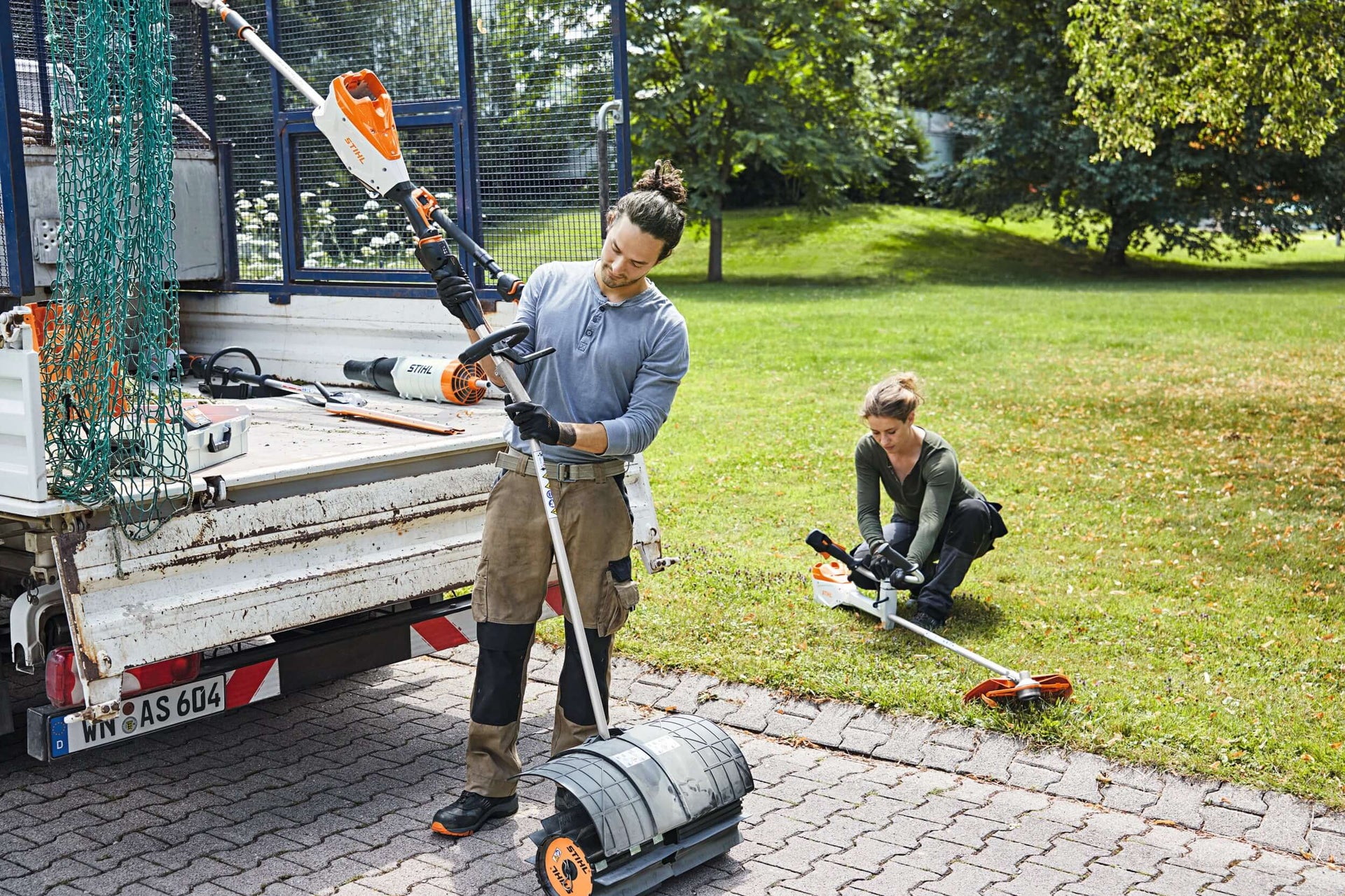 Two workers using STIHL MultiSystem tools in a garden, showcasing efficient lawn care and tree surgeon capabilities.
