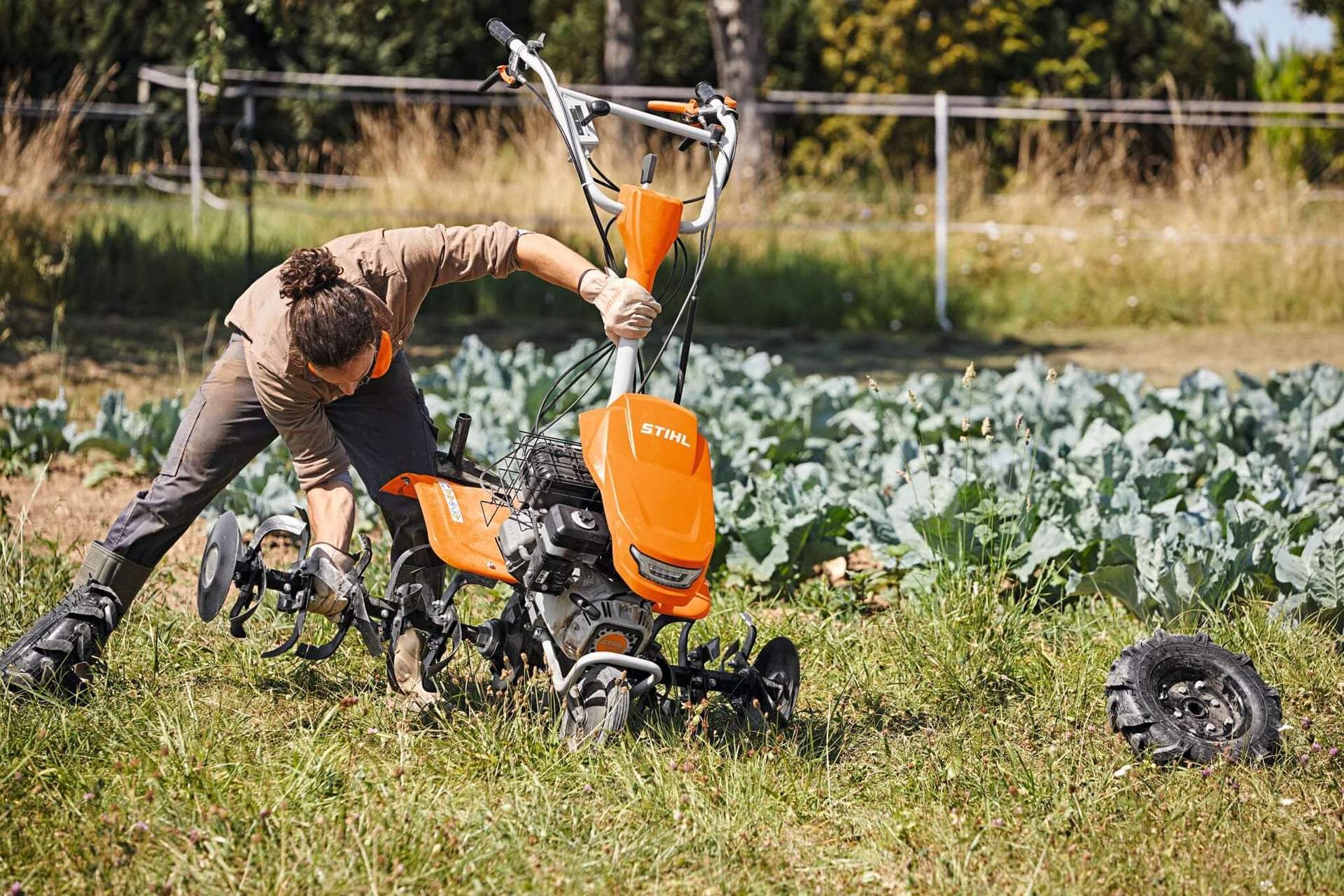 Person using a STIHL tiller in a garden, cultivating soil for planting vegetables.