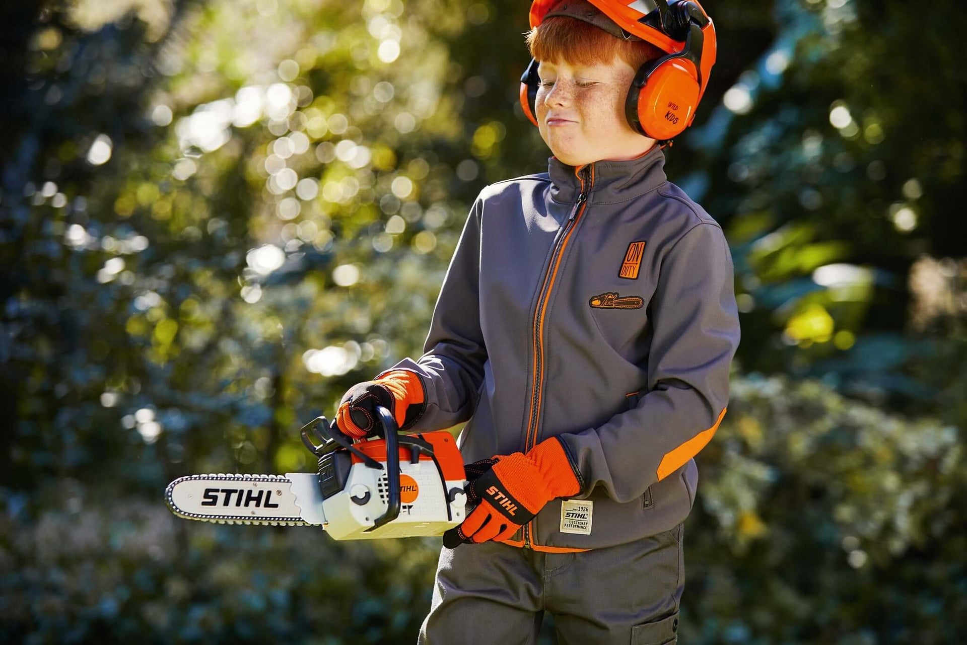 Young tree surgeon wearing protective gear and using a STIHL chainsaw in a garden setting.