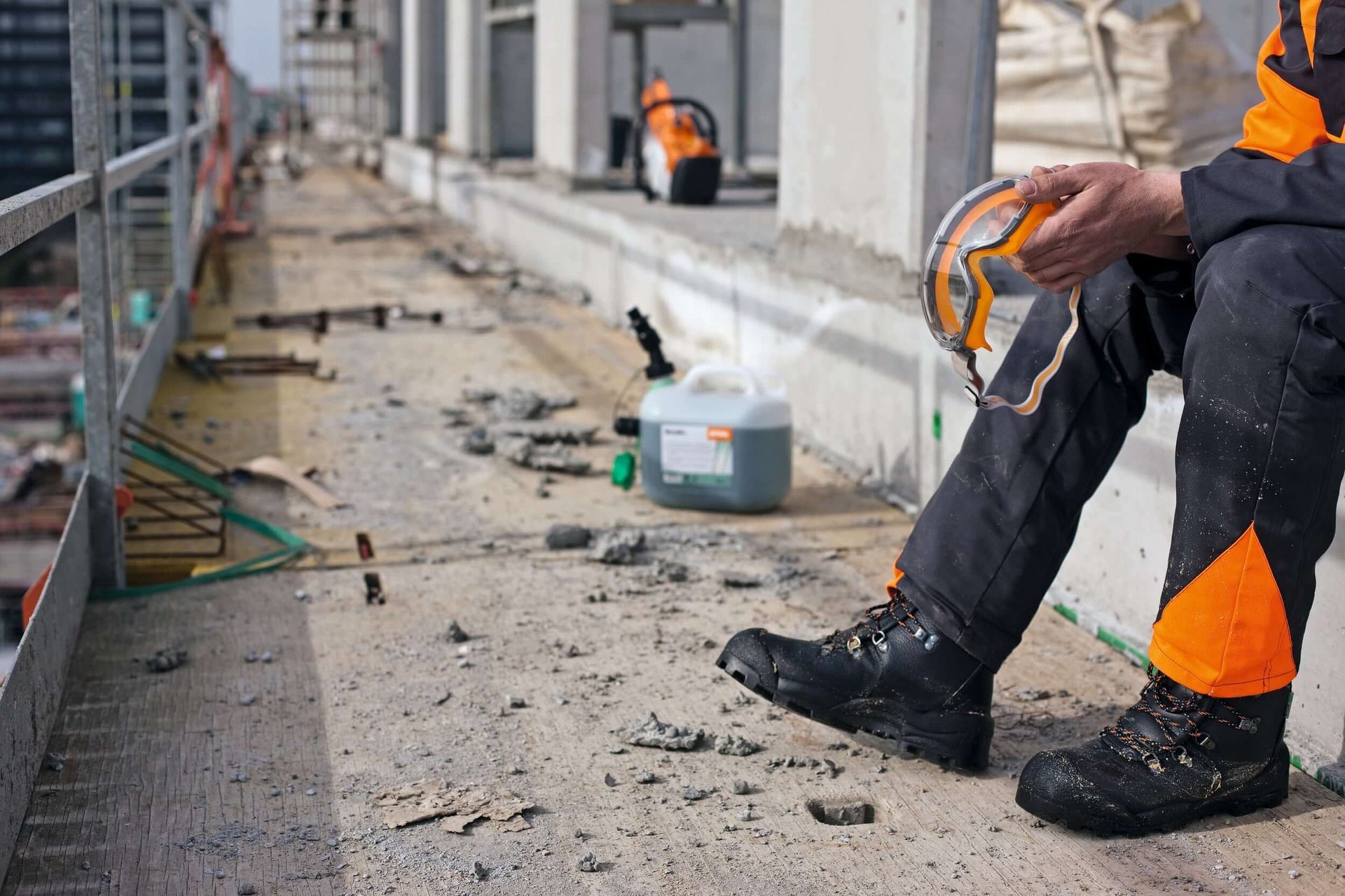 Construction worker resting on a job site, wearing safety gear and boots, with debris on the ground.