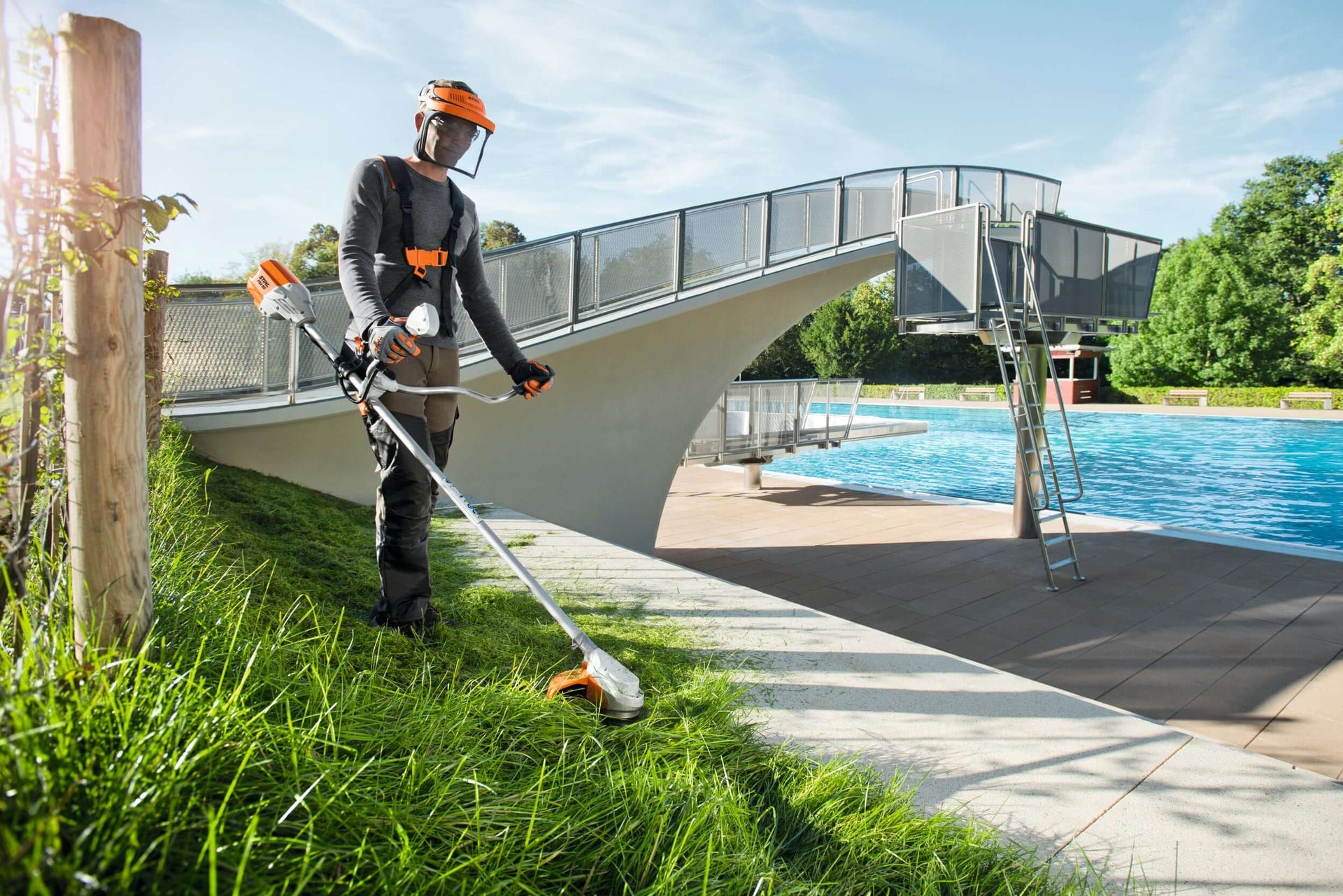 Professional with STIHL brushcutter trimming grass near a pool, showcasing effective vegetation management for tree surgeons.