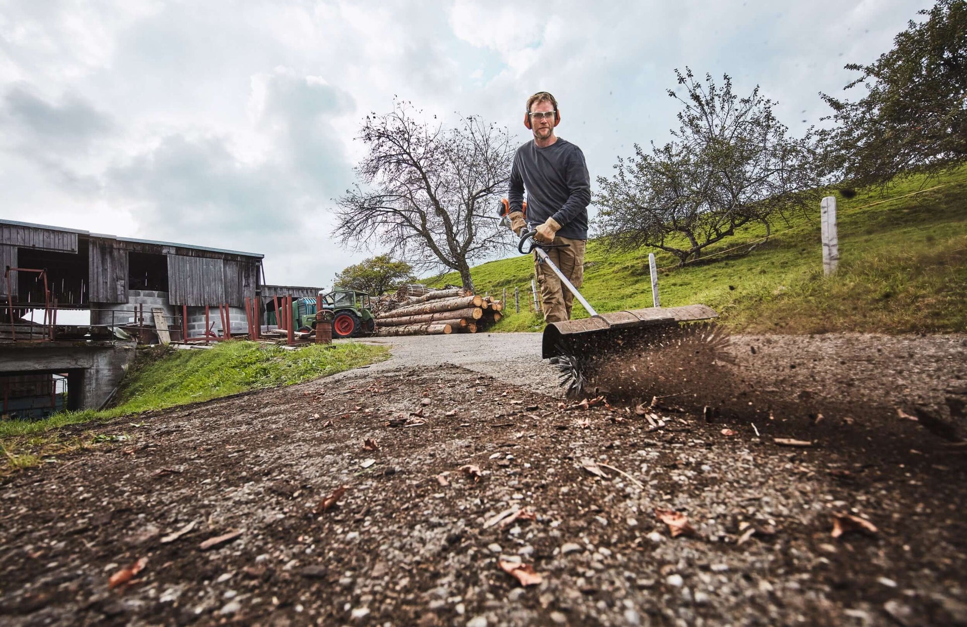 Man using a rake on a gravel path, showcasing garden maintenance with STIHL KombiSystem.