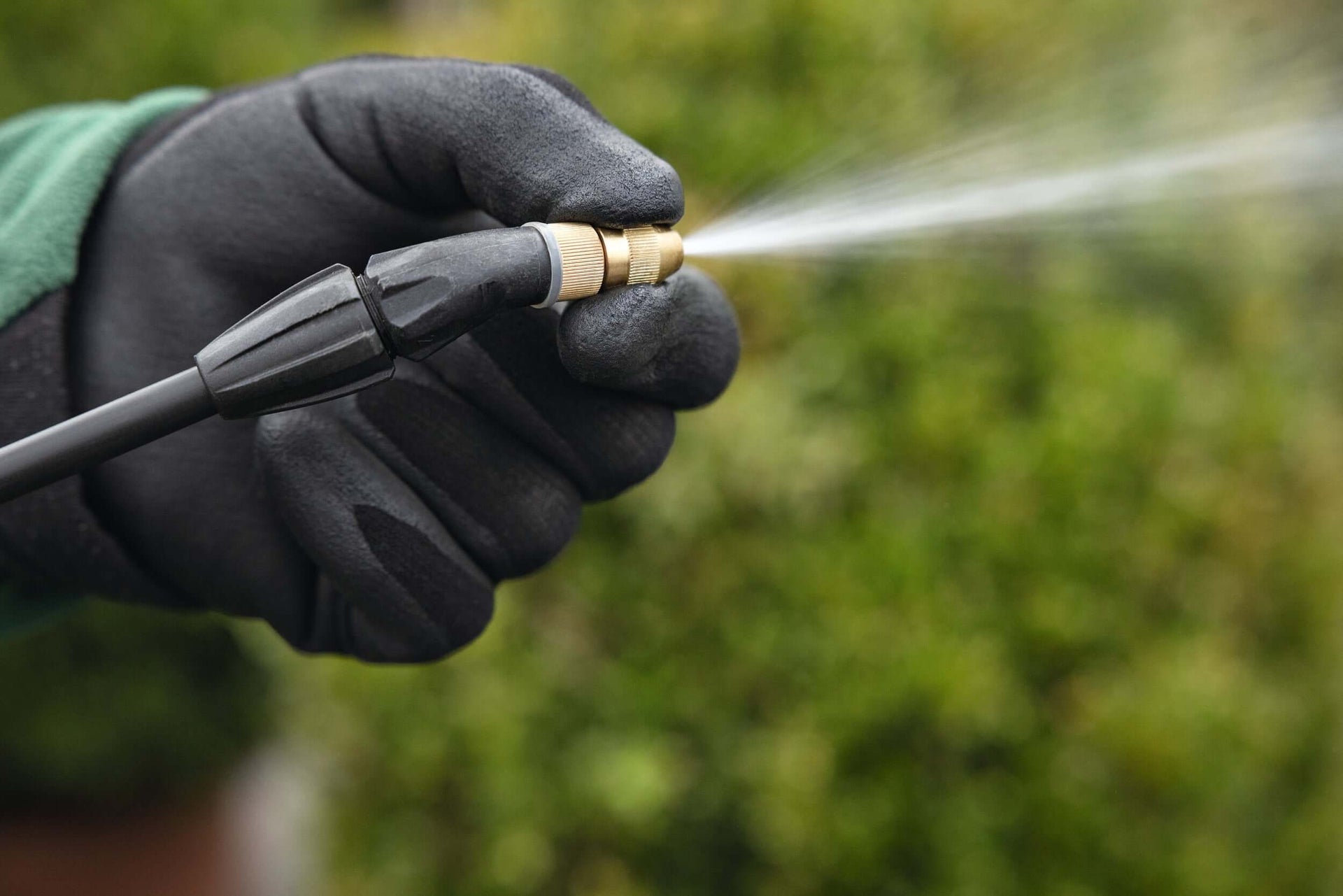 Close-up of a hand gripping a STIHL sprayer nozzle, showcasing precision tools for tree surgeons and gardening tasks.
