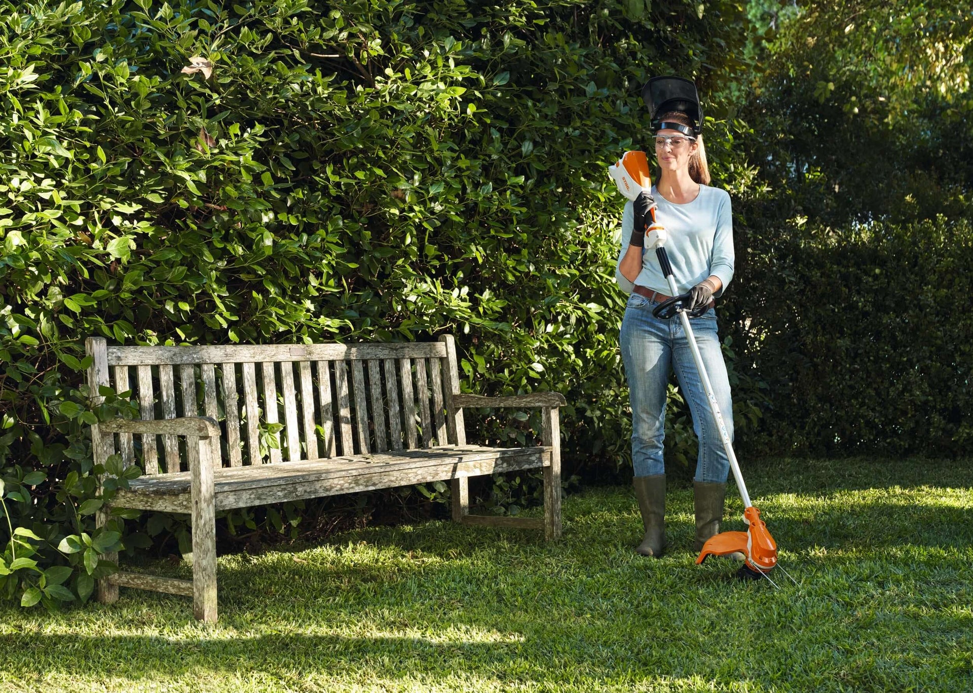 Woman using a STIHL grass trimmer in a garden, showcasing tools for effective lawn maintenance and garden care.