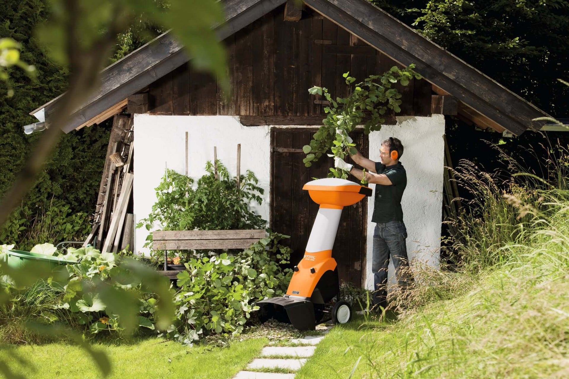 Tree surgeon using a STIHL garden shredder near a rustic shed, processing garden waste for compost.