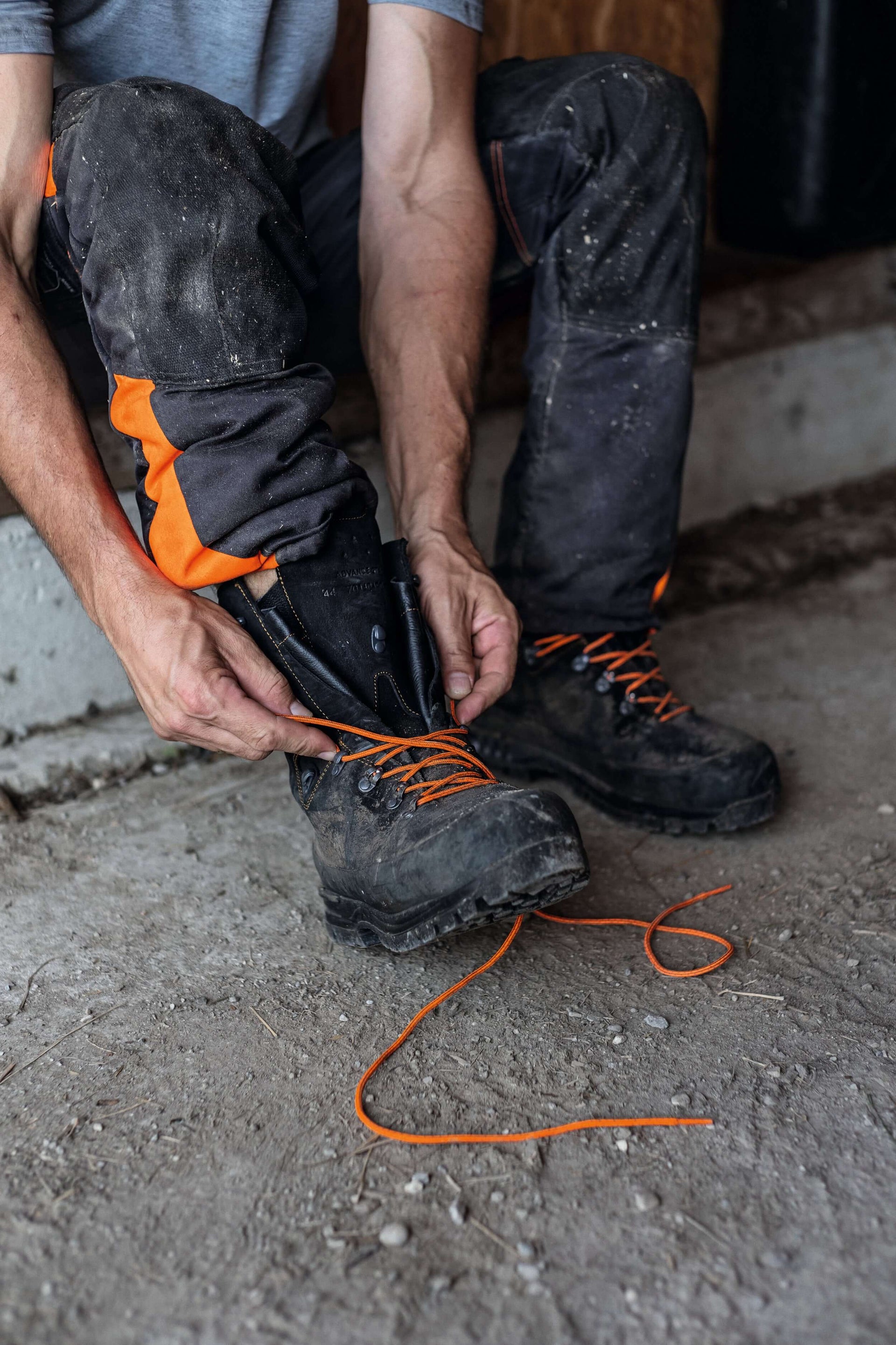 Tree surgeon tying orange replacement laces in black work boots, demonstrating high-performance footwear.