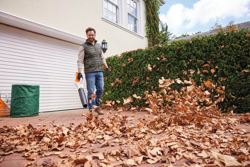 Man using STIHL BGA 50 cordless leaf blower to clear autumn leaves in a garden.