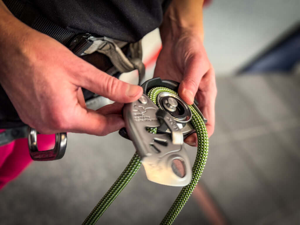 Close-up of a climber demonstrating a belay device and rope for safe tree surgery and climbing.