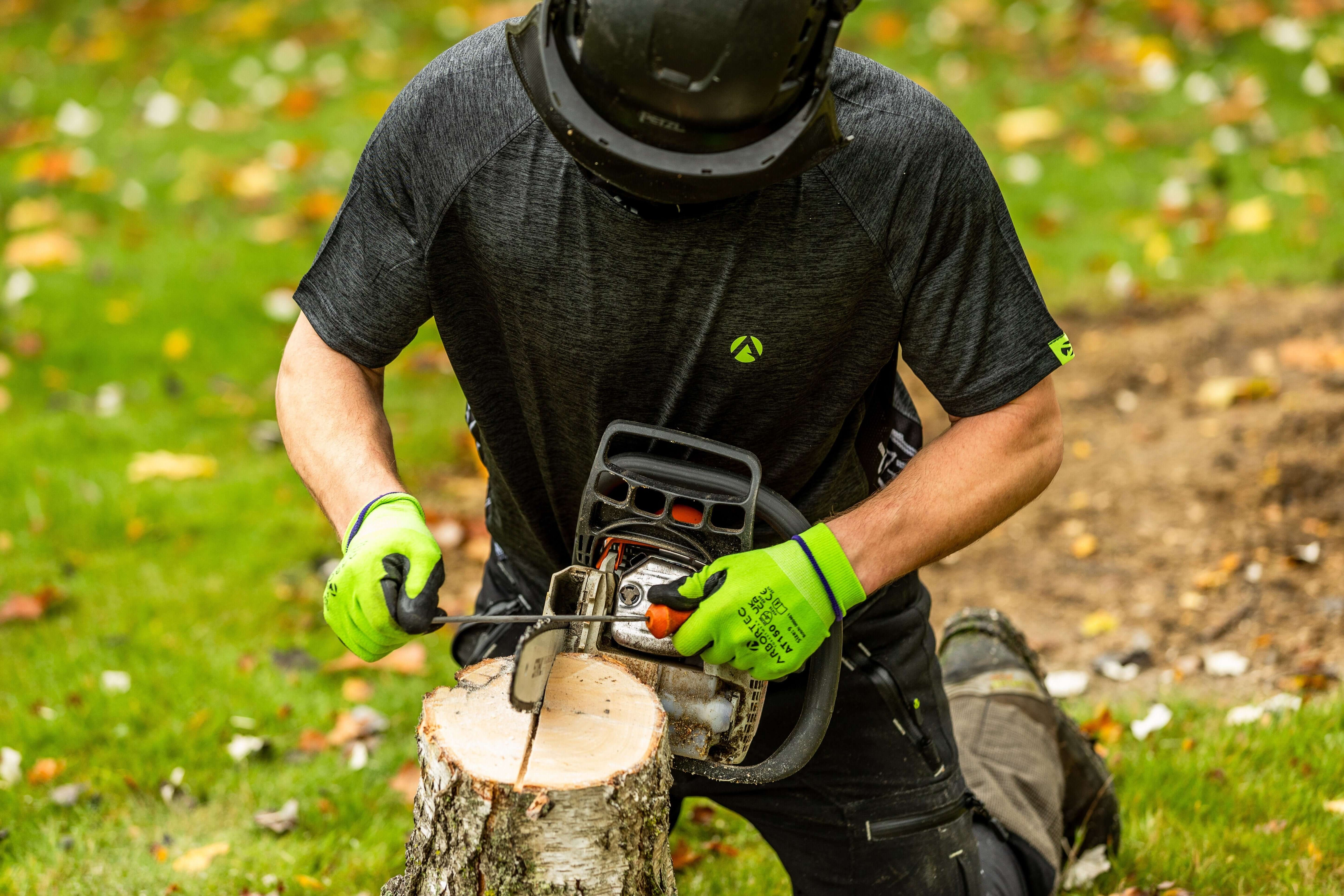 Arbortec T-Shirts worn by a tree surgeon using a chainsaw on a log outdoors, showcasing durability and comfort.