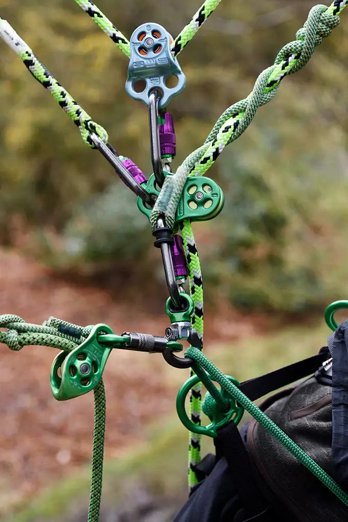 Close-up of a tree surgeon friction hitch climbing kit with colorful hardware and ropes, set in a natural environment.
