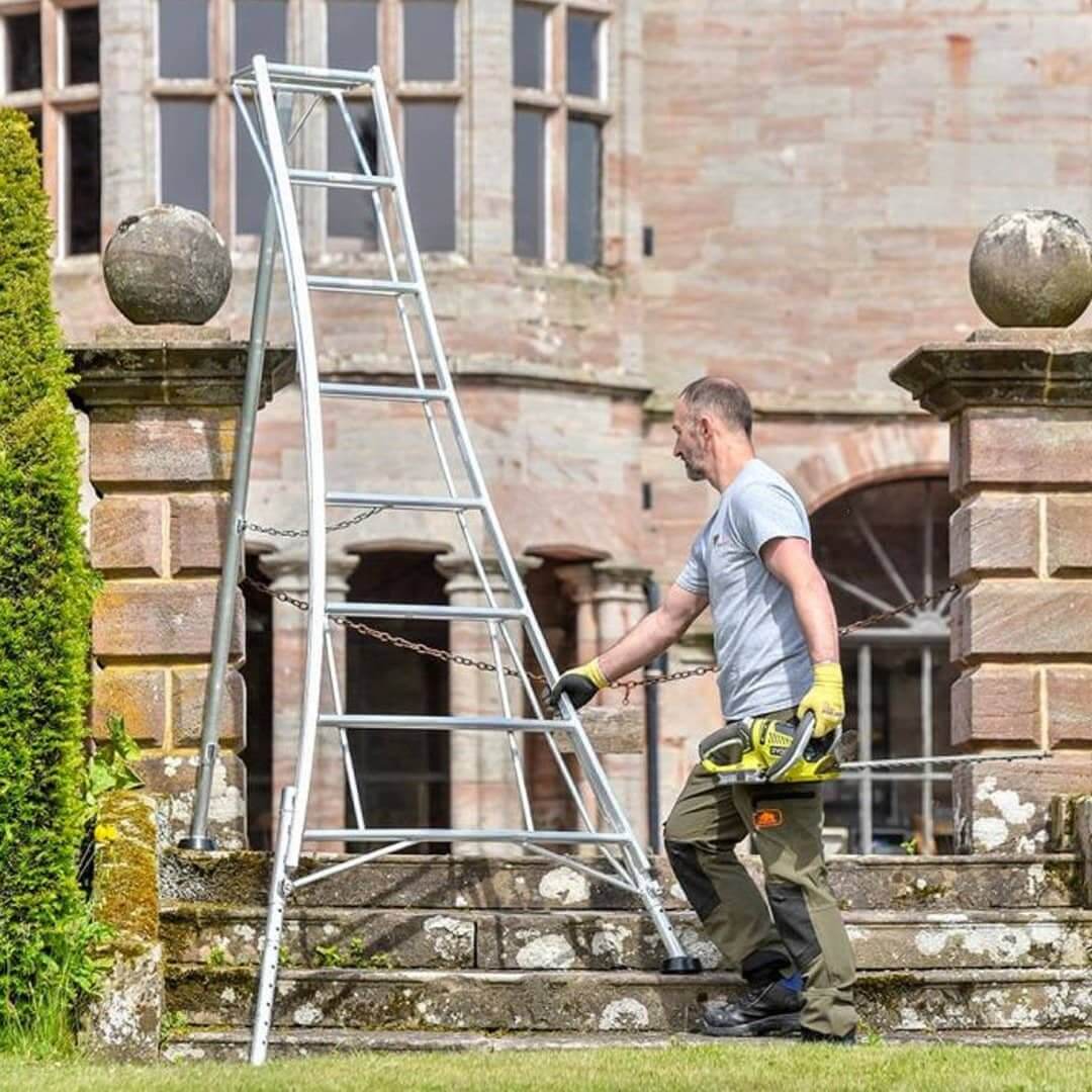 Tree surgeon using a Hendon tripod ladder for safe tree pruning on uneven ground.