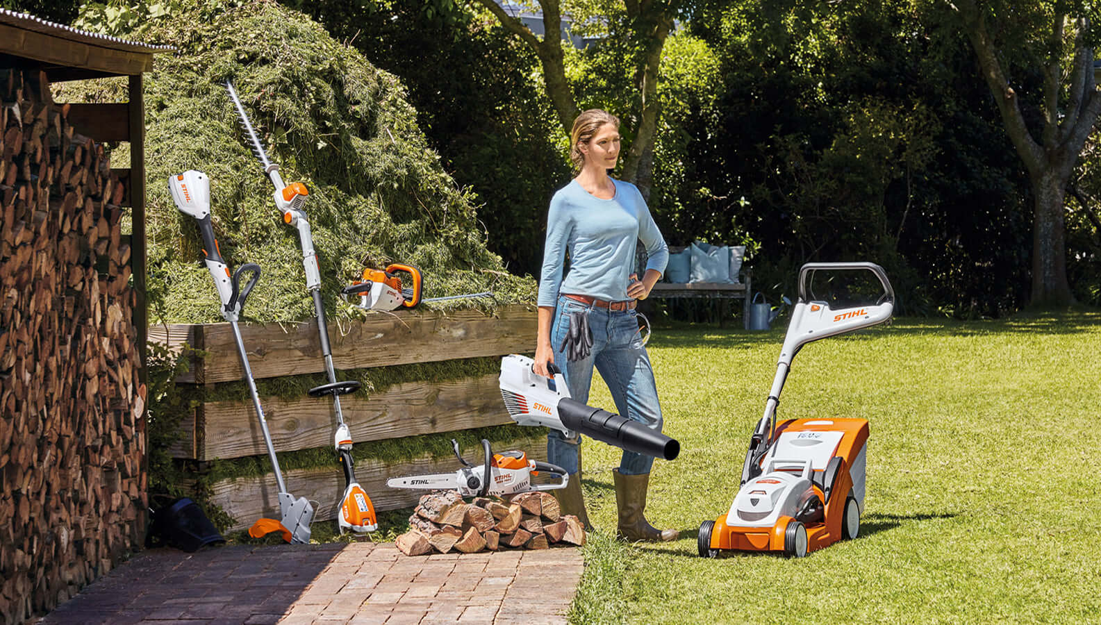 Woman using STIHL garden machinery, including hedge trimmers, leaf blower, and lawn mower, in a landscaped yard.