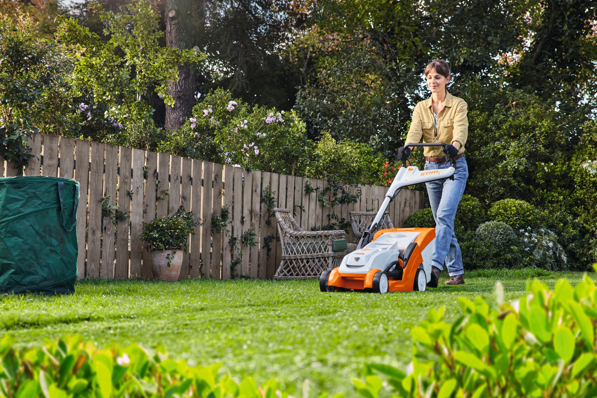 Woman using STIHL & Weibang Lawnmowers in a well-maintained garden, showing reliable cutting performance.