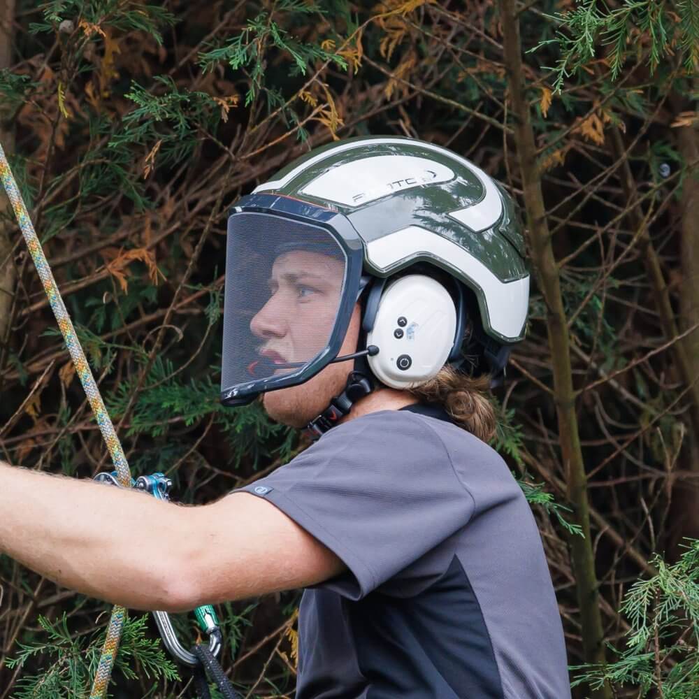 Tree surgeon wearing a safety helmet with visor while climbing a tree, highlighting safety and comfort in arboriculture.
