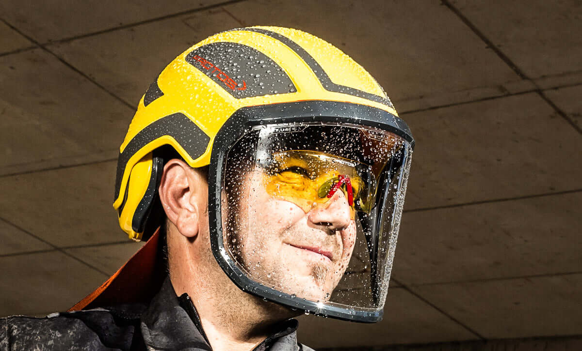 Yellow safety helmet with visor, worn by a tree surgeon, showcasing protection in wet conditions.