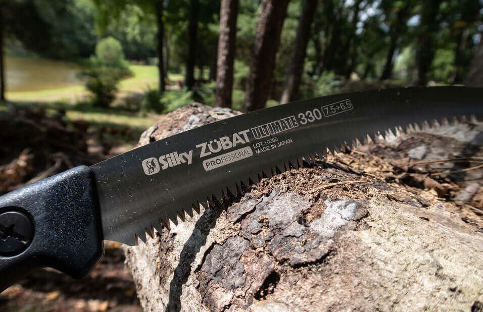 Close-up of Silky Zubat Ultimate 330 hand saw blade resting on a log, perfect for tree surgeons and garden maintenance.