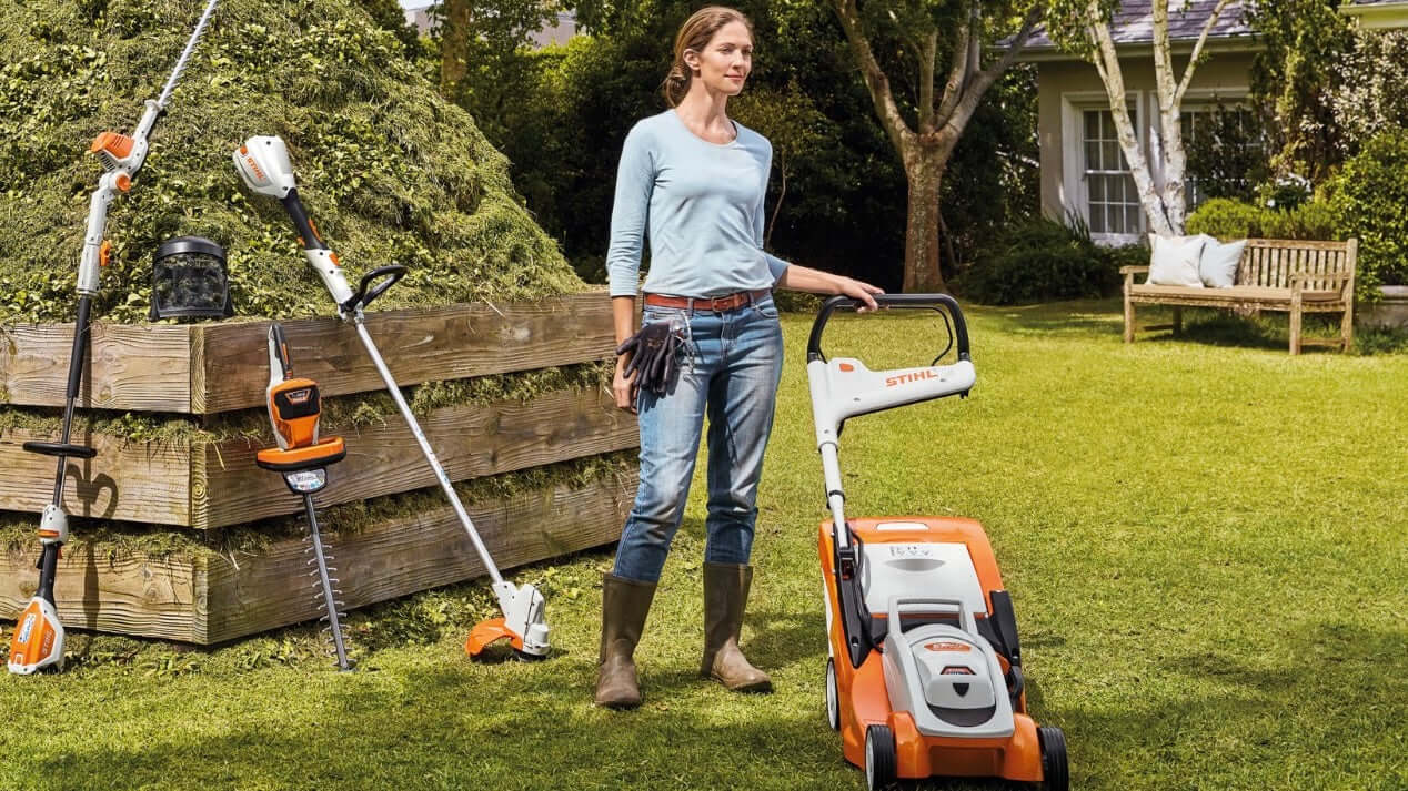 Woman using STIHL lawn mower in a well-kept garden, surrounded by gardening tools and equipment.