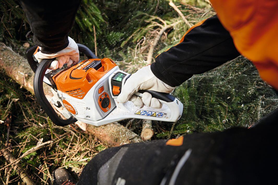 User operating the MSA 300 Cordless Battery Chainsaw for professional tree surgery in a forest setting.