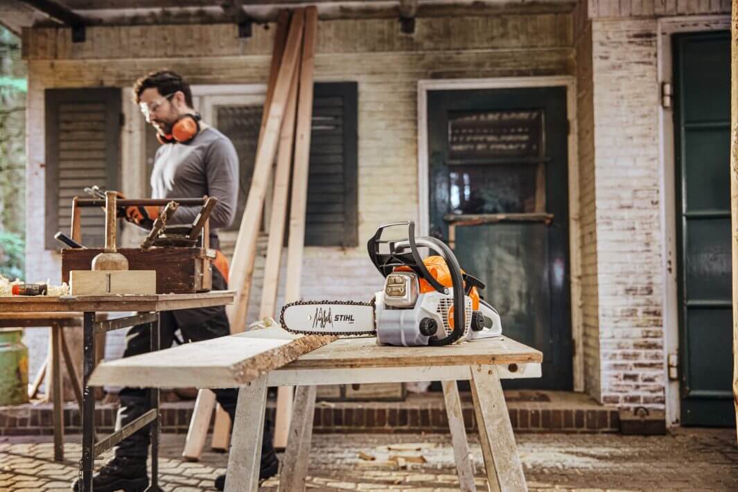STIHL MS 162 petrol chainsaw on a workbench with a carpenter, ideal for tree surgeons and outdoor projects.
