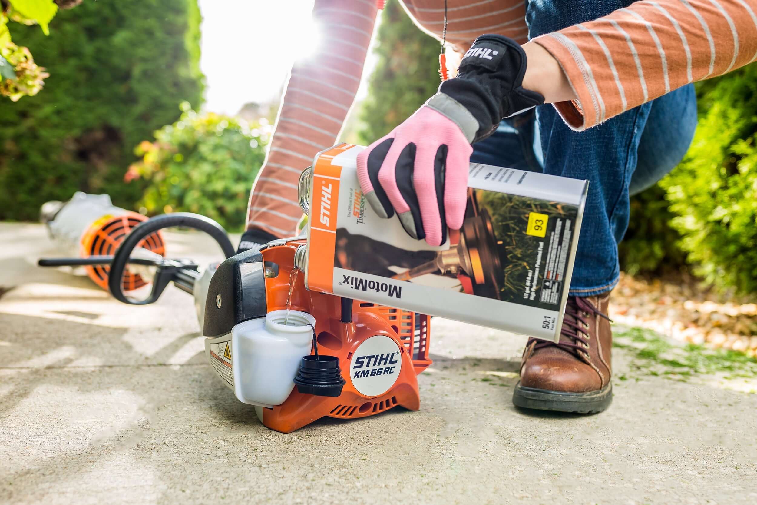 A person in gloves pouring STIHL MotoMix fuel into a STIHL trimmer, ensuring optimal performance for tree surgeons.