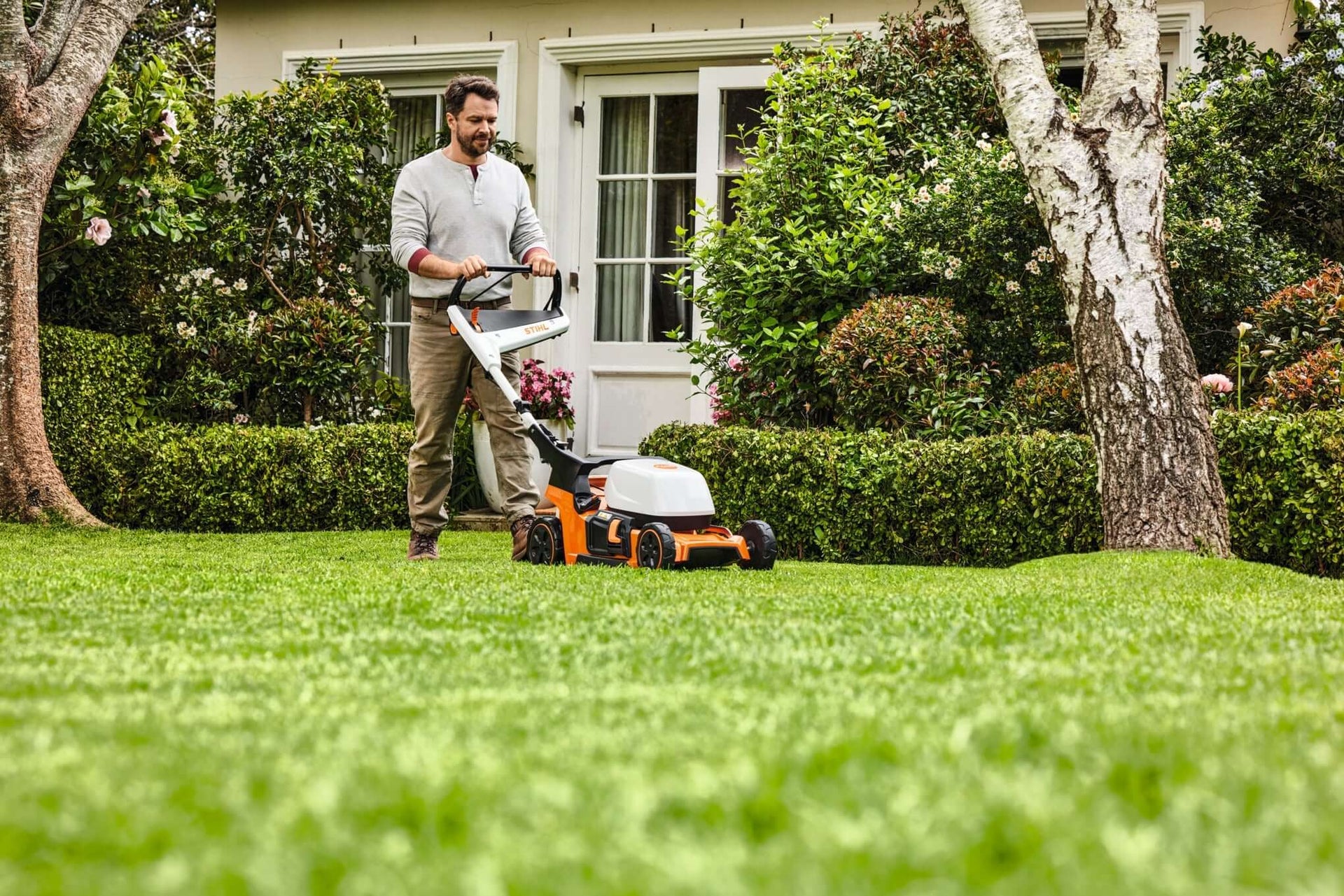 Man using a STIHL mulching lawnmower in a lush green garden for healthy lawn maintenance.