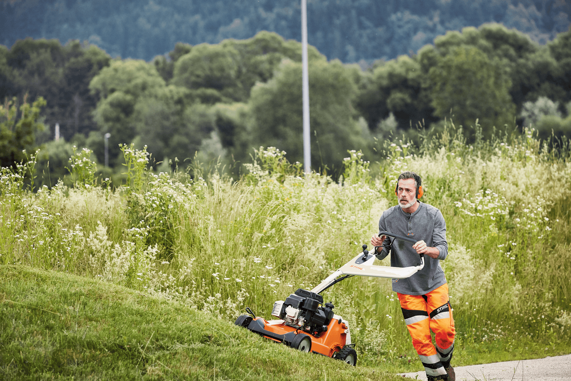 A tree surgeon using a professional STIHL lawn mower in a lush green landscape.