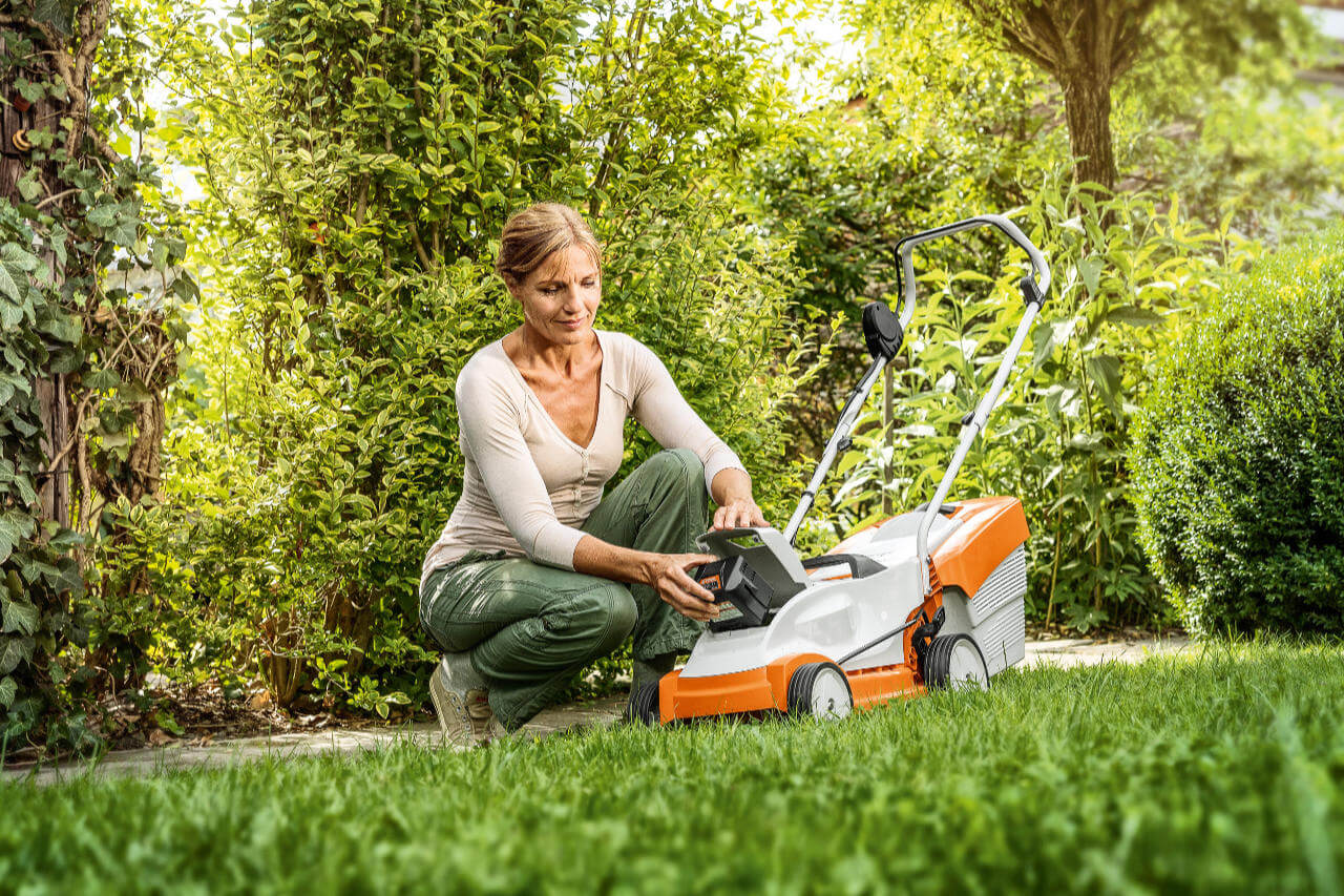 Woman adjusting STIHL small lawnmower in lush garden, ideal for maintaining small to medium lawns.