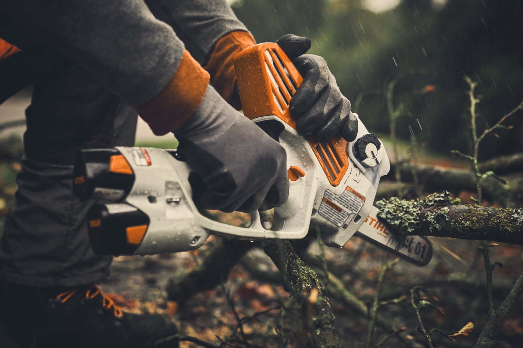 Tree surgeon using STIHL battery chainsaw on fallen branch in a forest, showcasing cordless garden machinery.