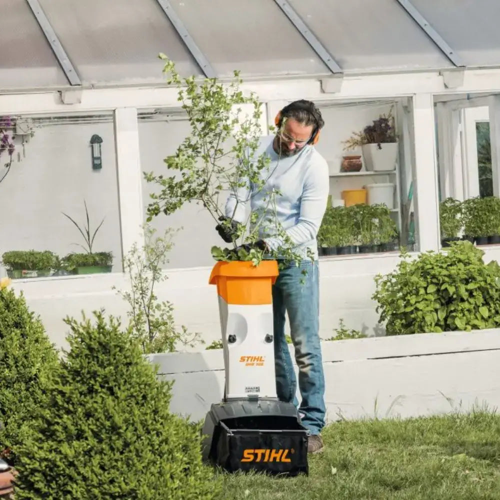 Man using STIHL garden shredder to dispose of branches in a well-maintained garden, showcasing effective waste management.