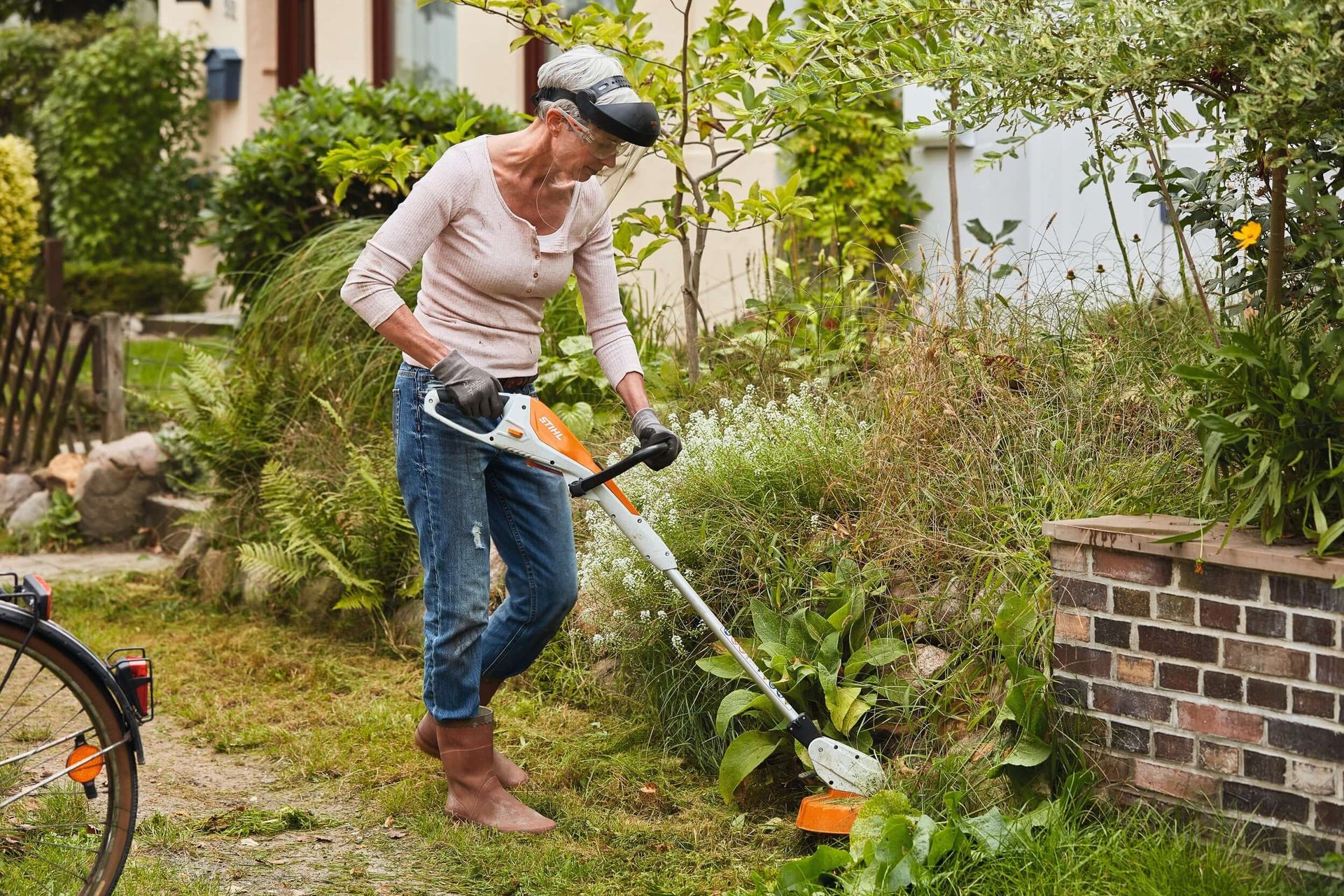 Woman using STIHL AI battery-powered trimmer for effortless gardening in a lush backyard.