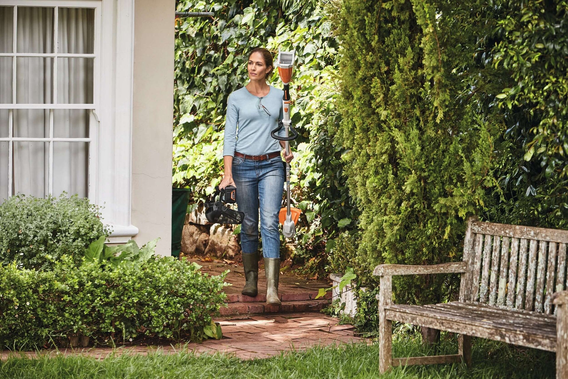 A woman using STIHL AK Battery tools in a lush garden, ready for tree surgery and landscaping tasks.