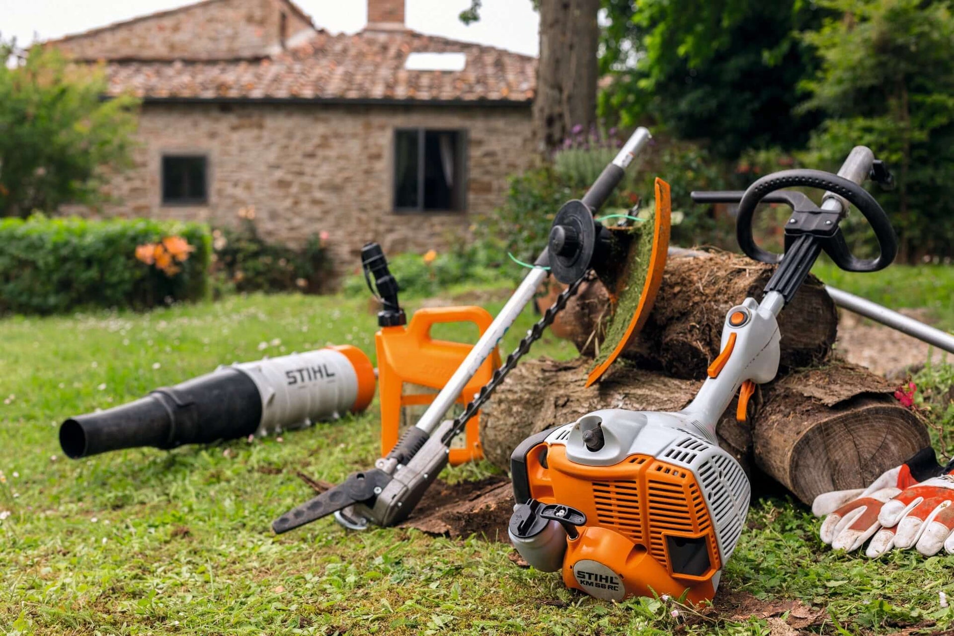STIHL Kombi attachments for garden maintenance, including tree surgeon tools, placed on a lawn with a rustic backdrop.