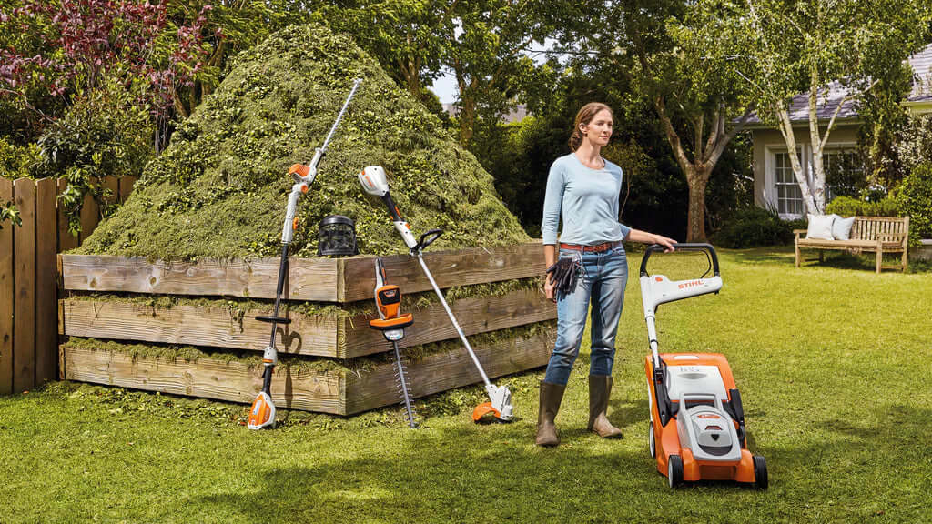 Woman standing with STIHL garden tools near a pile of grass clippings, ideal for Tree Surgeons and home gardening.
