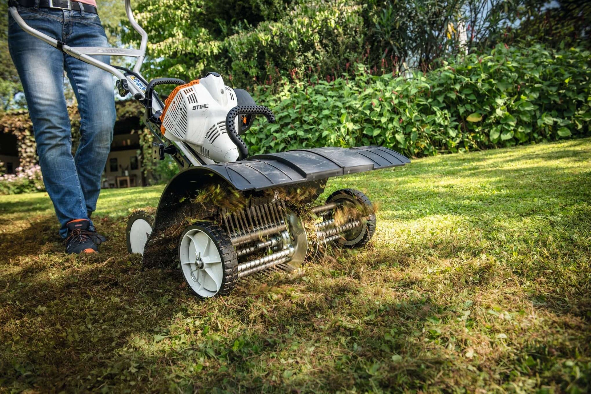 Person using STIHL Multi System dethatcher attachment on a lush lawn, promoting effective lawn care and maintenance.