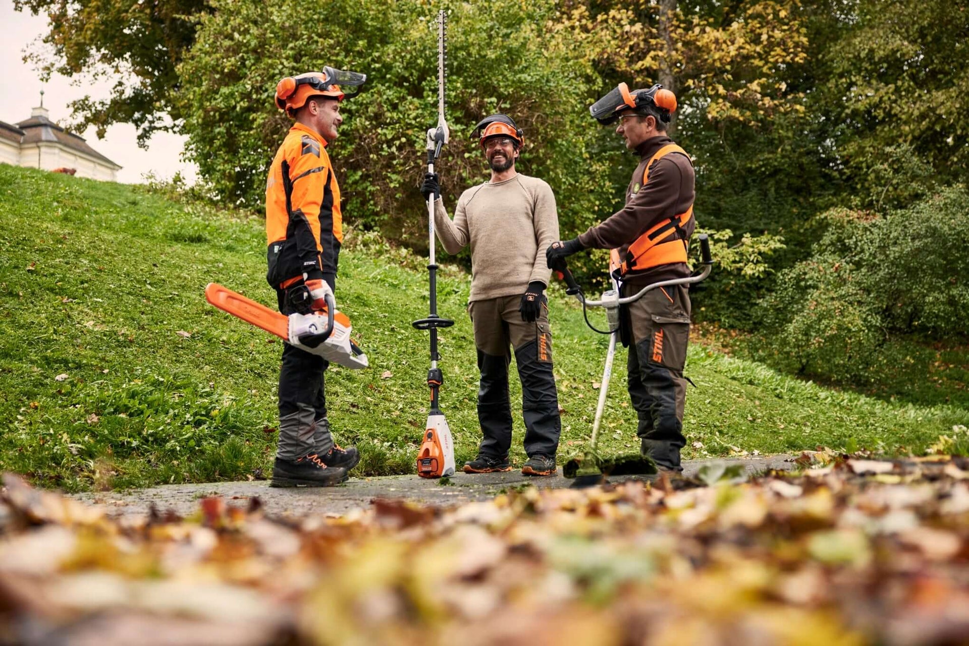 Three tree surgeons in STIHL gear discussing outdoor power tools amidst autumn leaves.