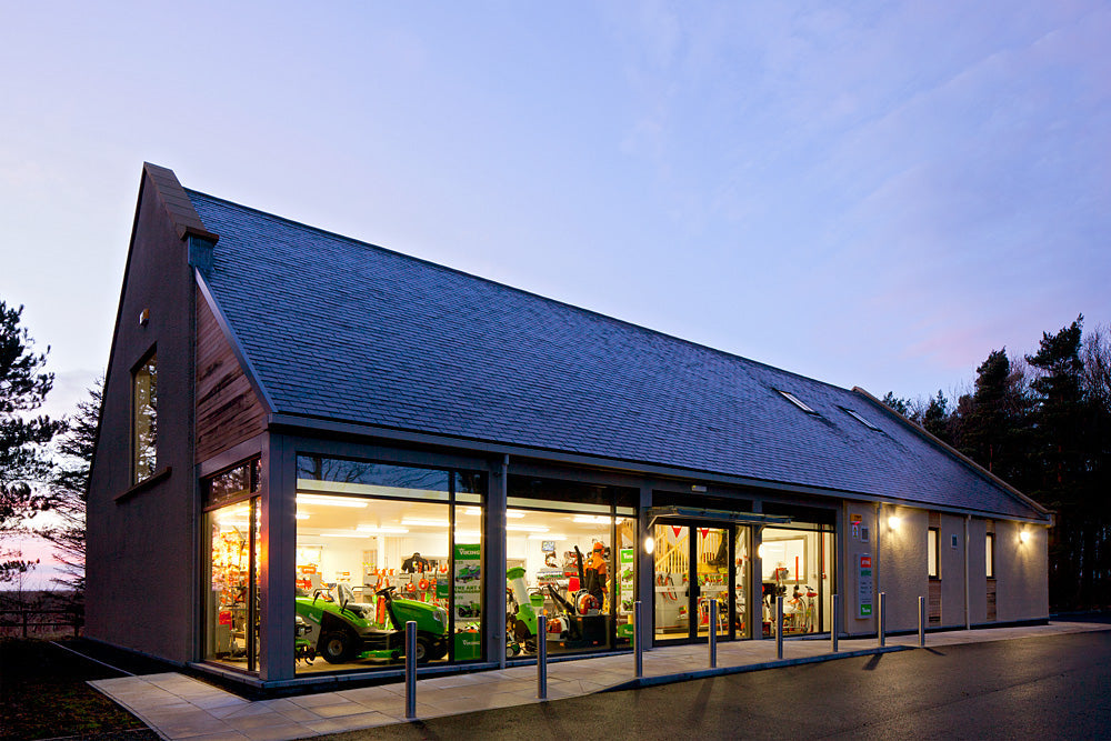 Gustharts store showcasing tree surgery and gardening machinery, with a modern facade at dusk.