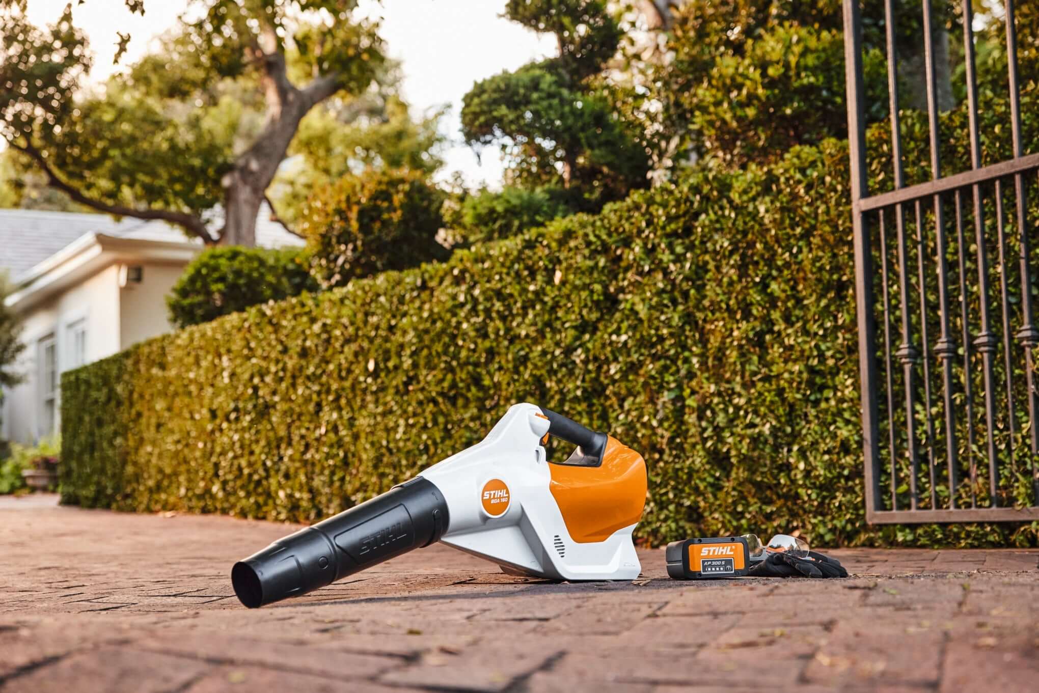 STIHL cordless leaf blower resting beside a neatly trimmed hedge, offering a quiet and efficient garden clearing solution.
