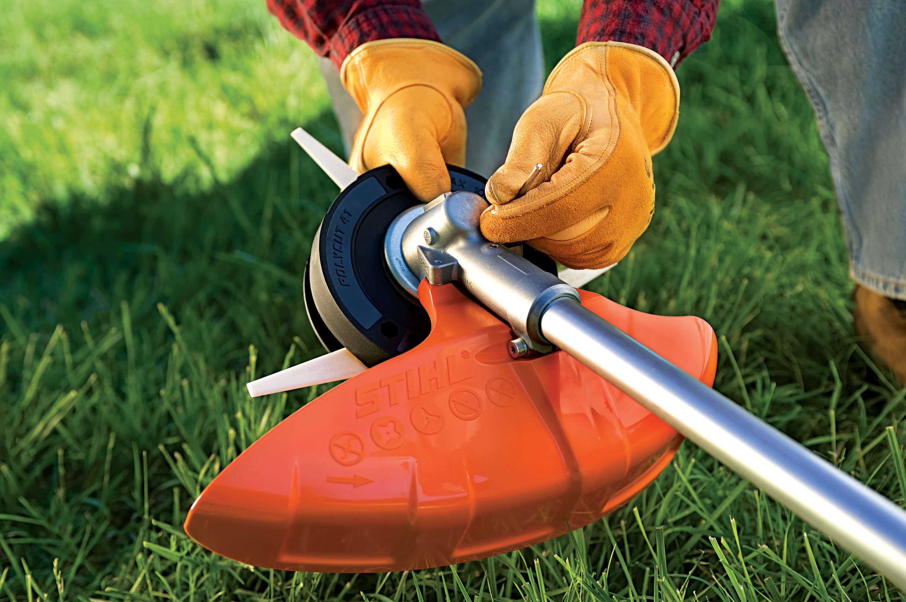 Tree surgeon adjusting a STIHL mowing blade on a brushcutter, demonstrating precise grass trimming techniques.