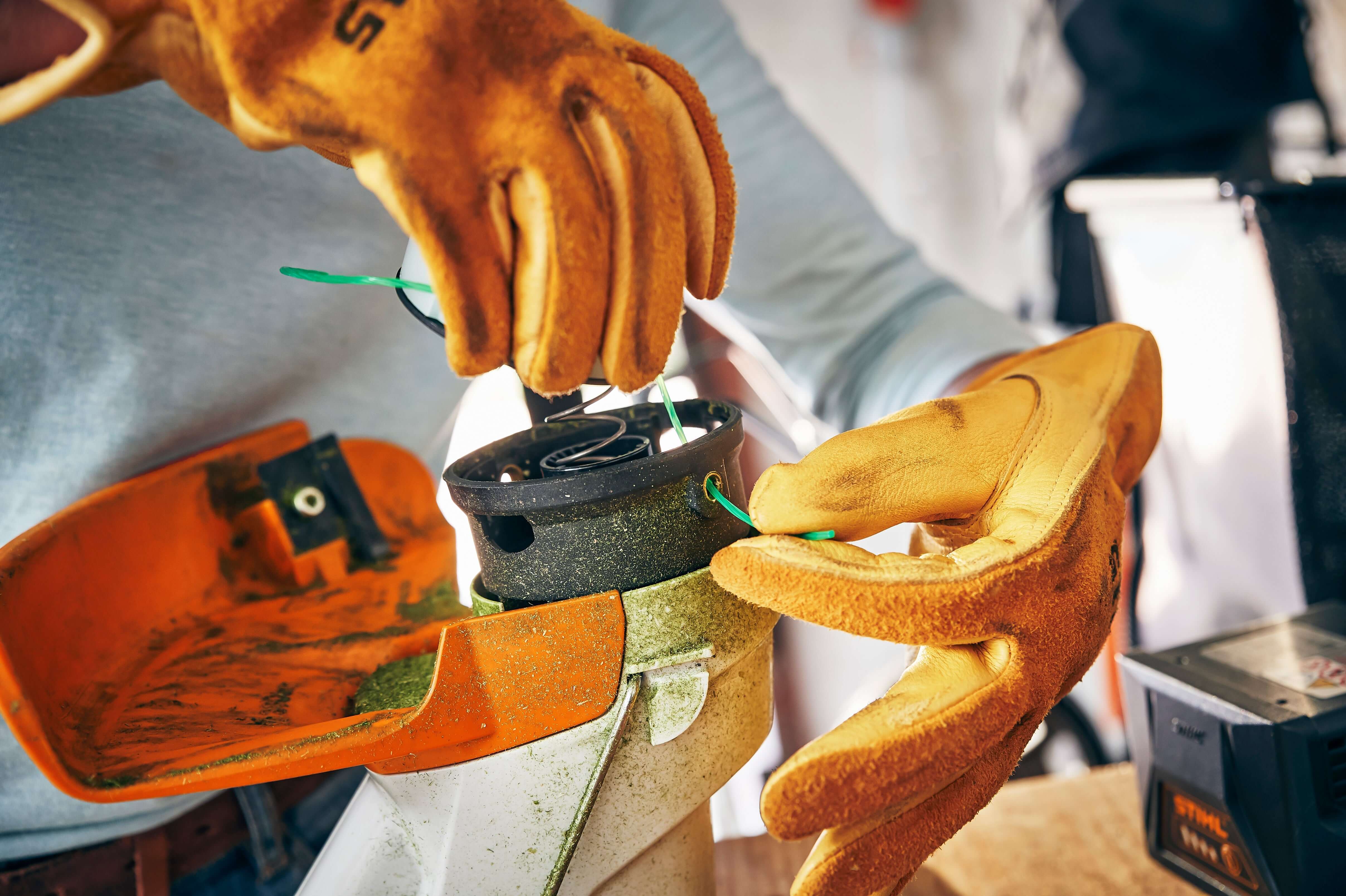 Person replacing STIHL mowing line in strimmer, wearing protective gloves for safety and efficiency.